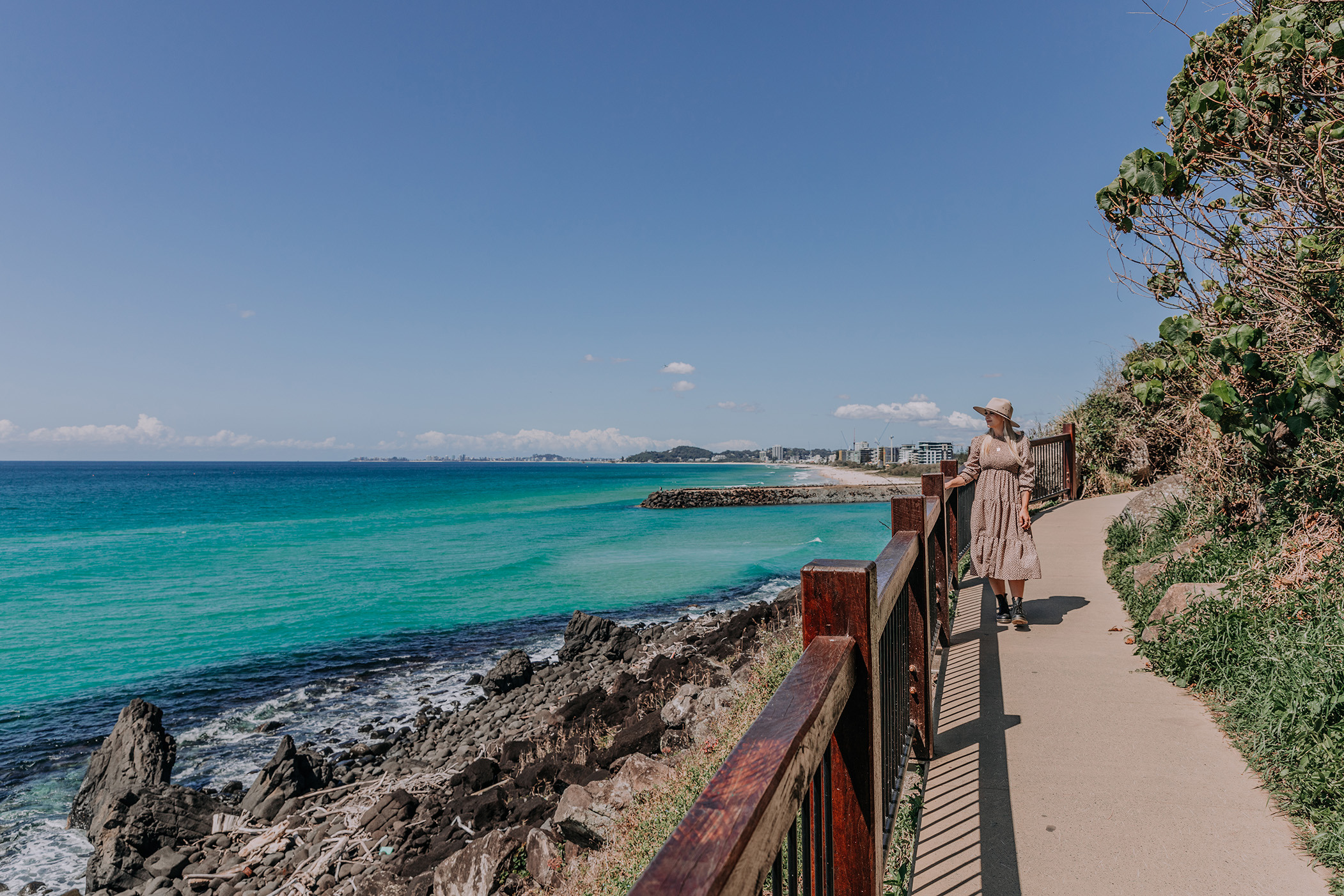 A woman walks along the ocean view path around Burleigh Headland on a sunny day.