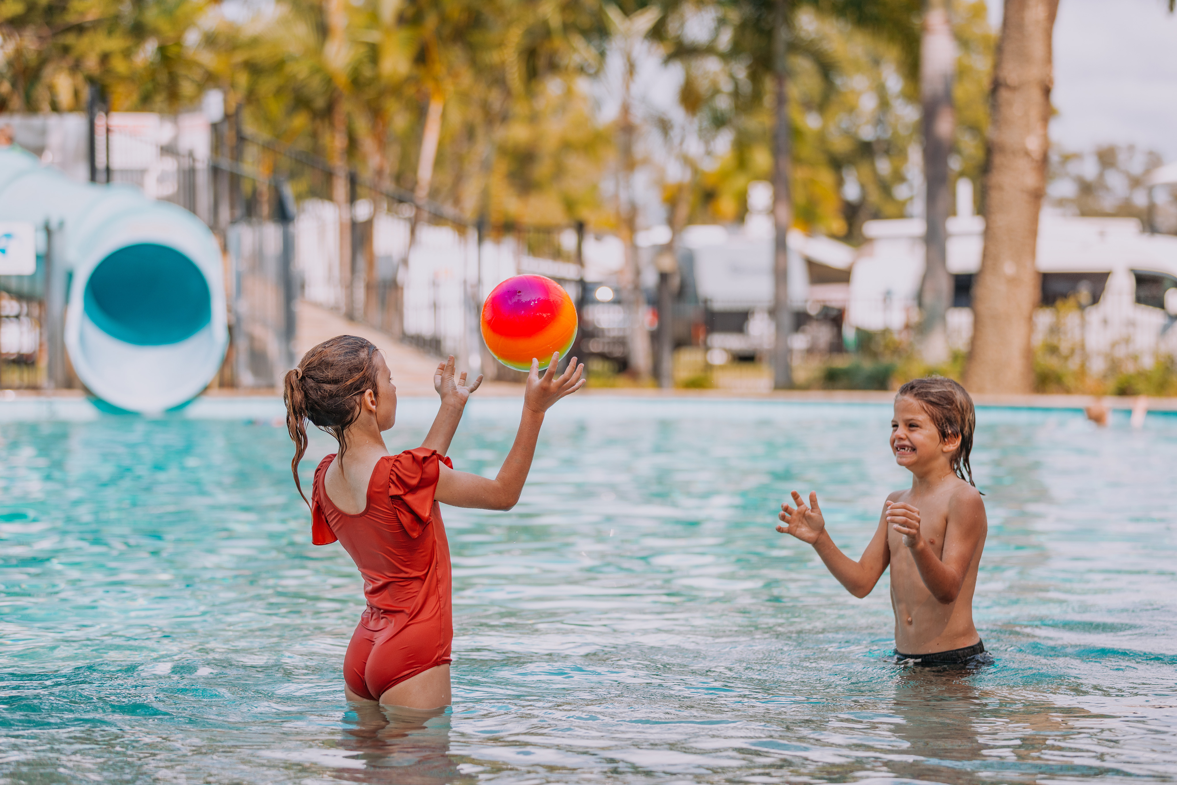 Two young kids tossing a ball back and forth in a shallow swimming pool at Tallebudgera Creek Tourist Park.
