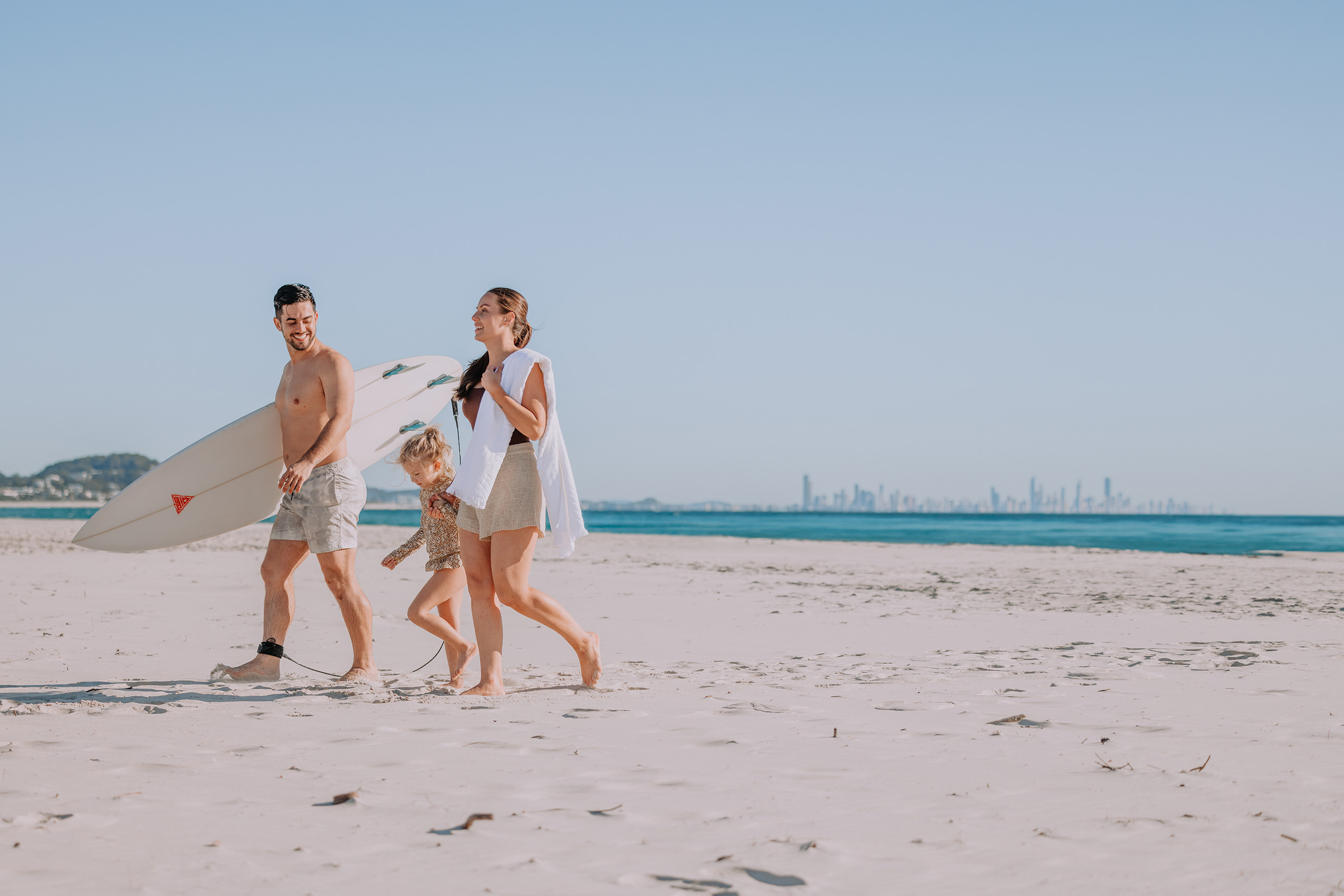 A family of three walking along the beach with a surfboard at Kirra.