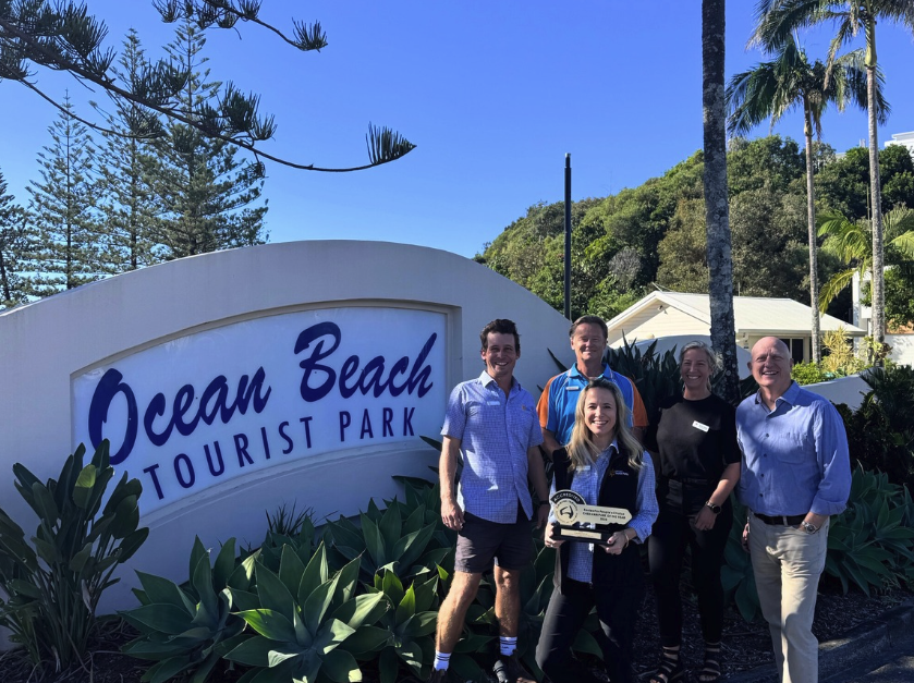 Ocean Beach staff members stand near the park entry sign, holding their award.