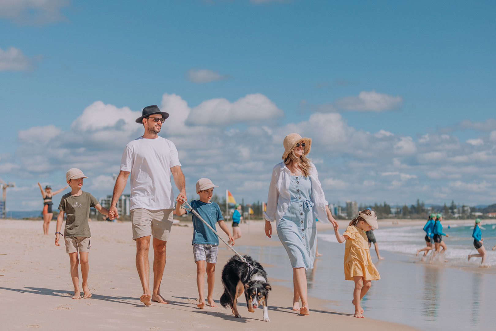 Family walking along the beach with their dog, the background has the skyline of the Gold Coast